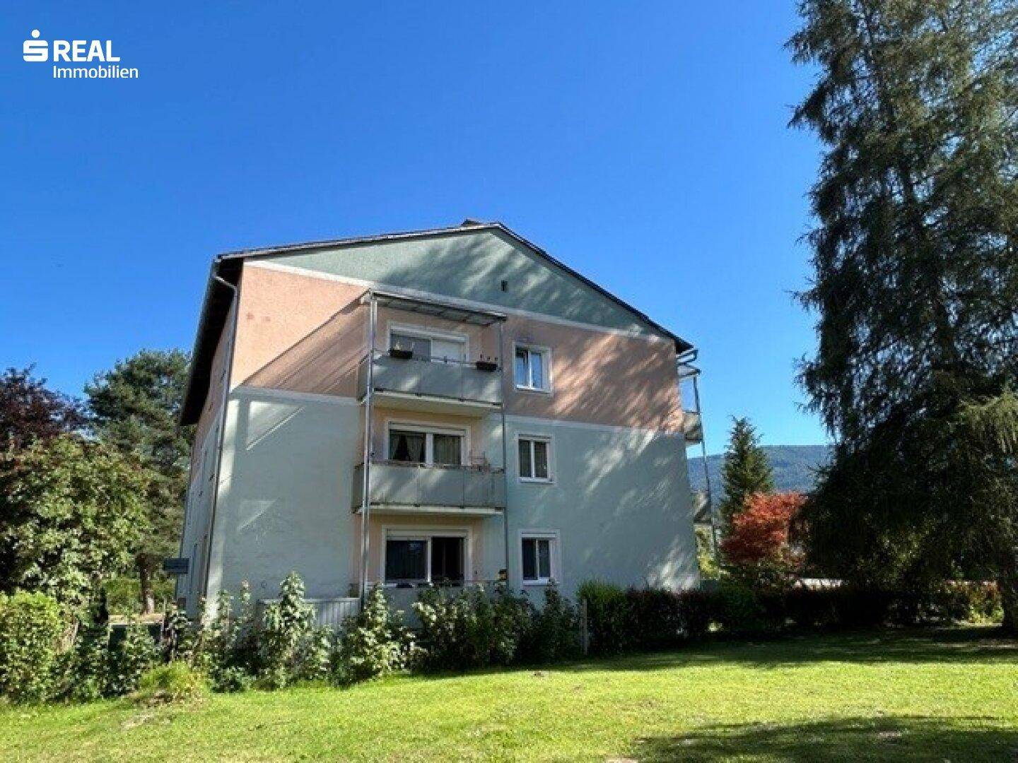 Seitenansicht des Wohnhauses mit Balkonen und umgebender Grünfläche.