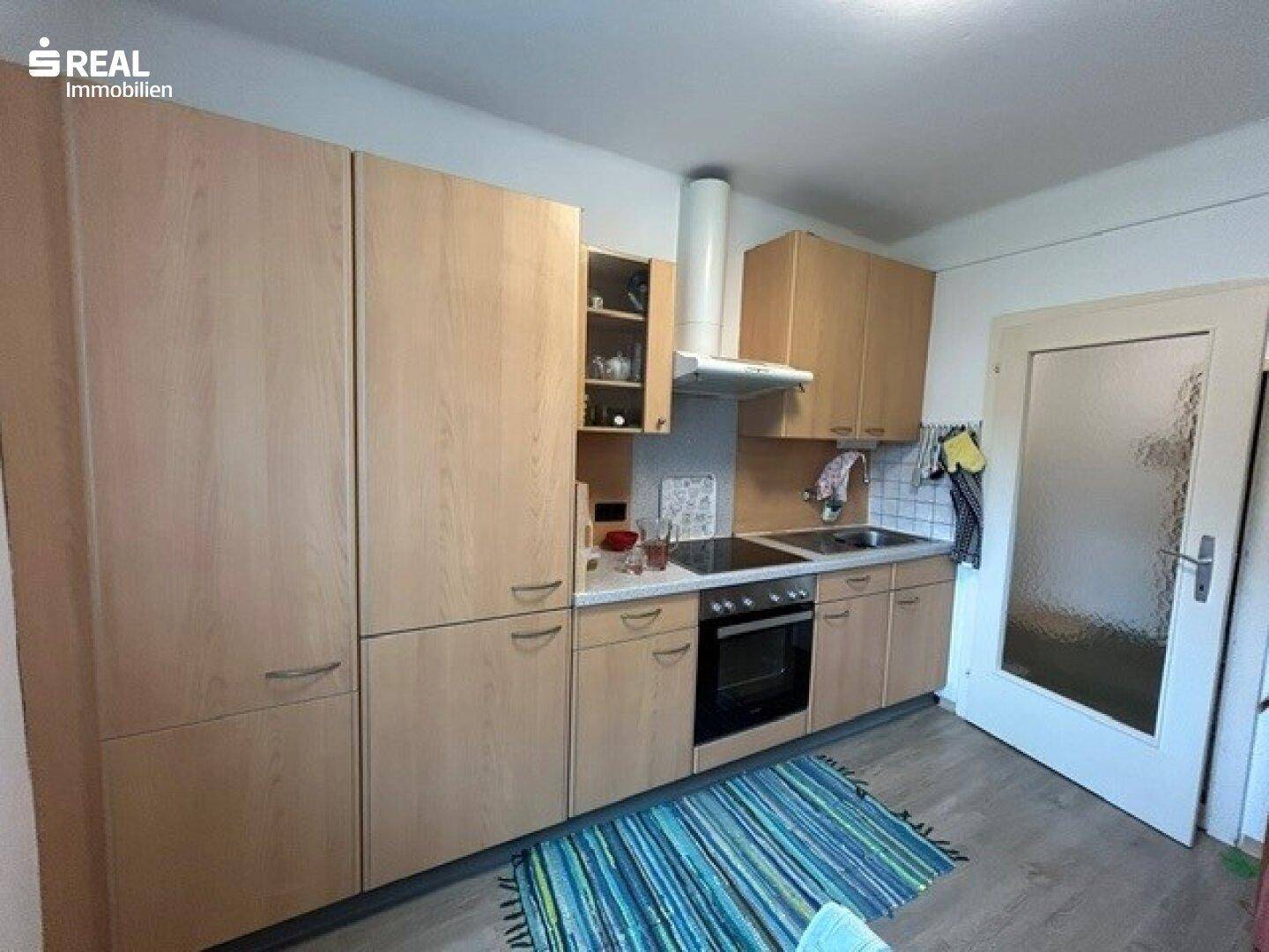 Funktionale Küche mit Holzschränken, Kochfeld und Dunstabzugshaube.