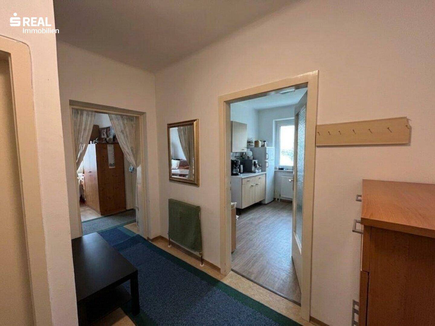 Flur mit Teppichboden und Blick in die Küche sowie weitere Zimmer.