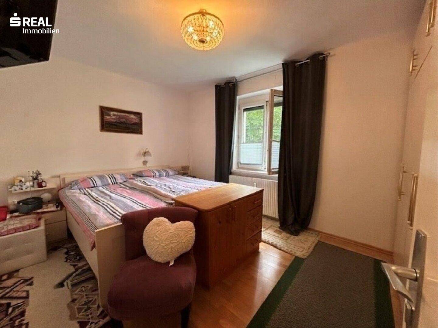 Schlafzimmer mit Doppelbett, Holzmöbeln und Fenster mit dunklen Vorhängen.