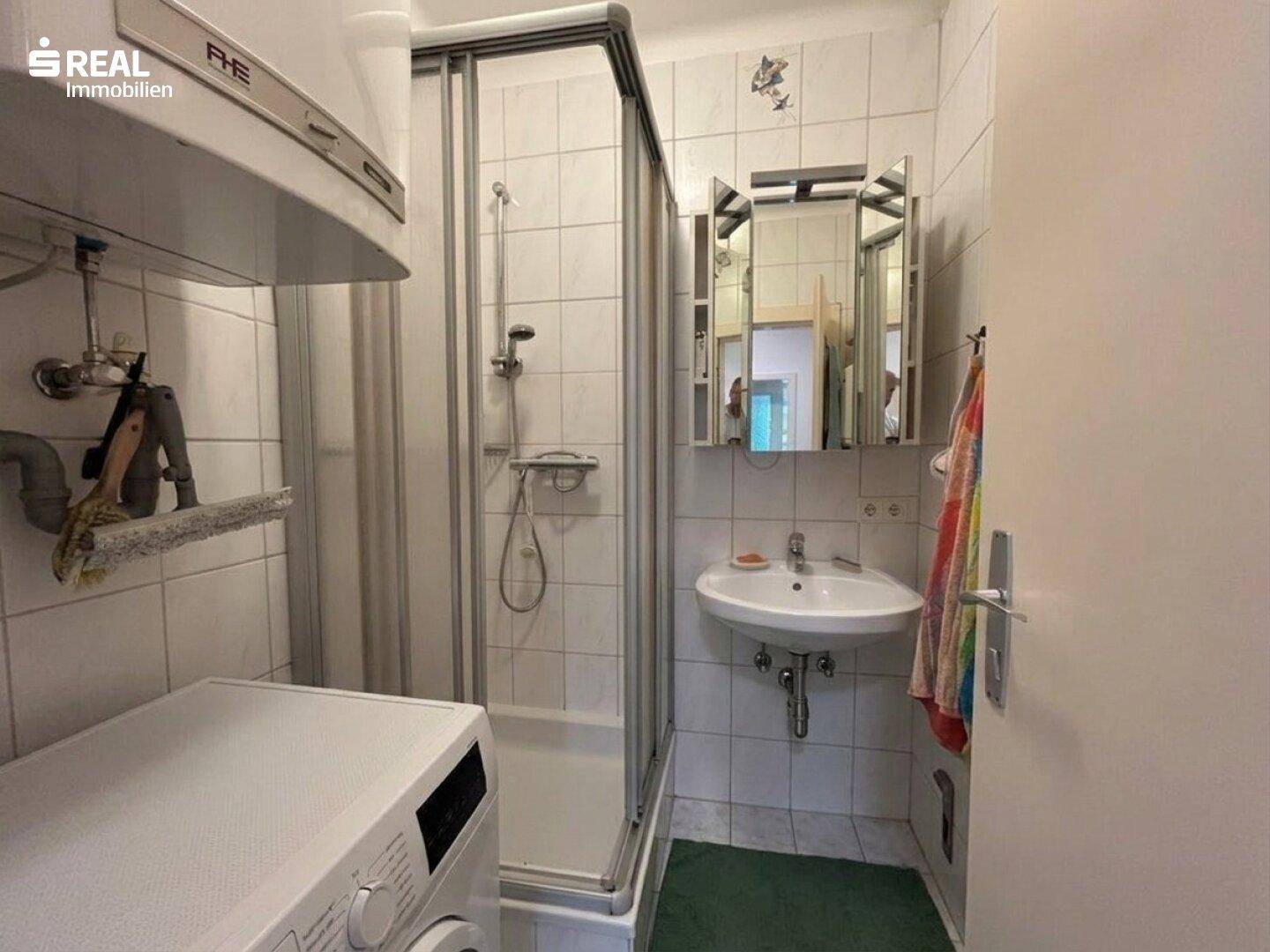 Badezimmer mit Duschkabine, Waschbecken und Waschmaschine.
