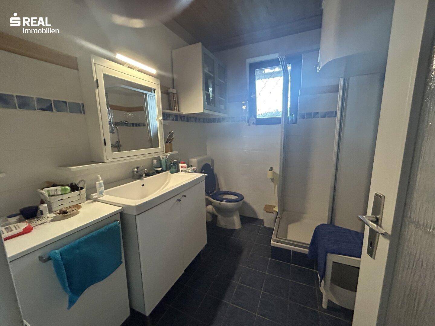 Badezimmer mit Dusche, Waschbecken, WC und Fenster, in gutem Zustand.