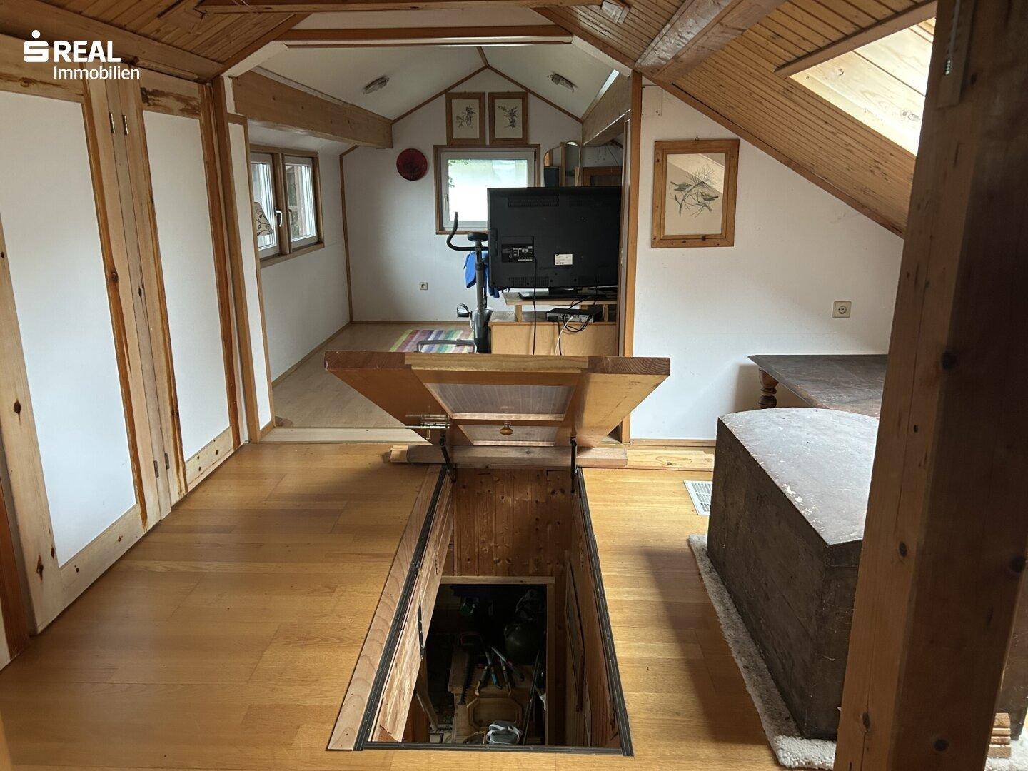 Dachboden mit Holzboden, sichtbaren Balken und Zugang zu einem weiteren Raum.