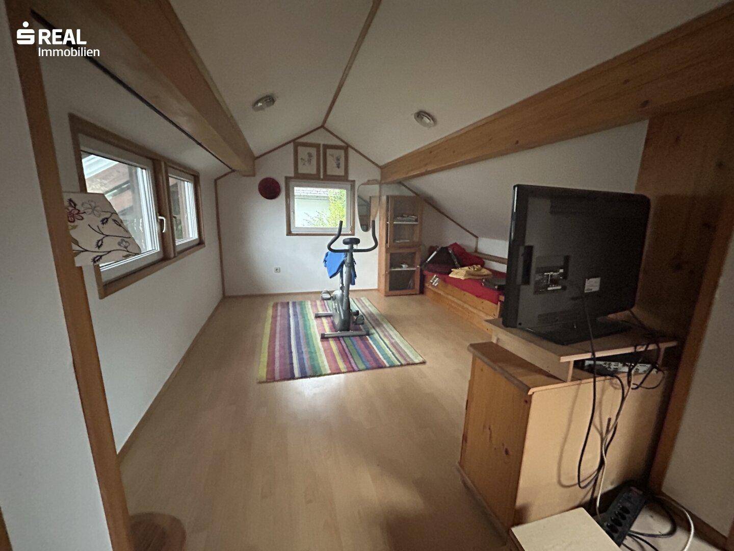 Ausgebauter Dachboden mit Holzbalken, Laminatboden und Fitnessgerät.
