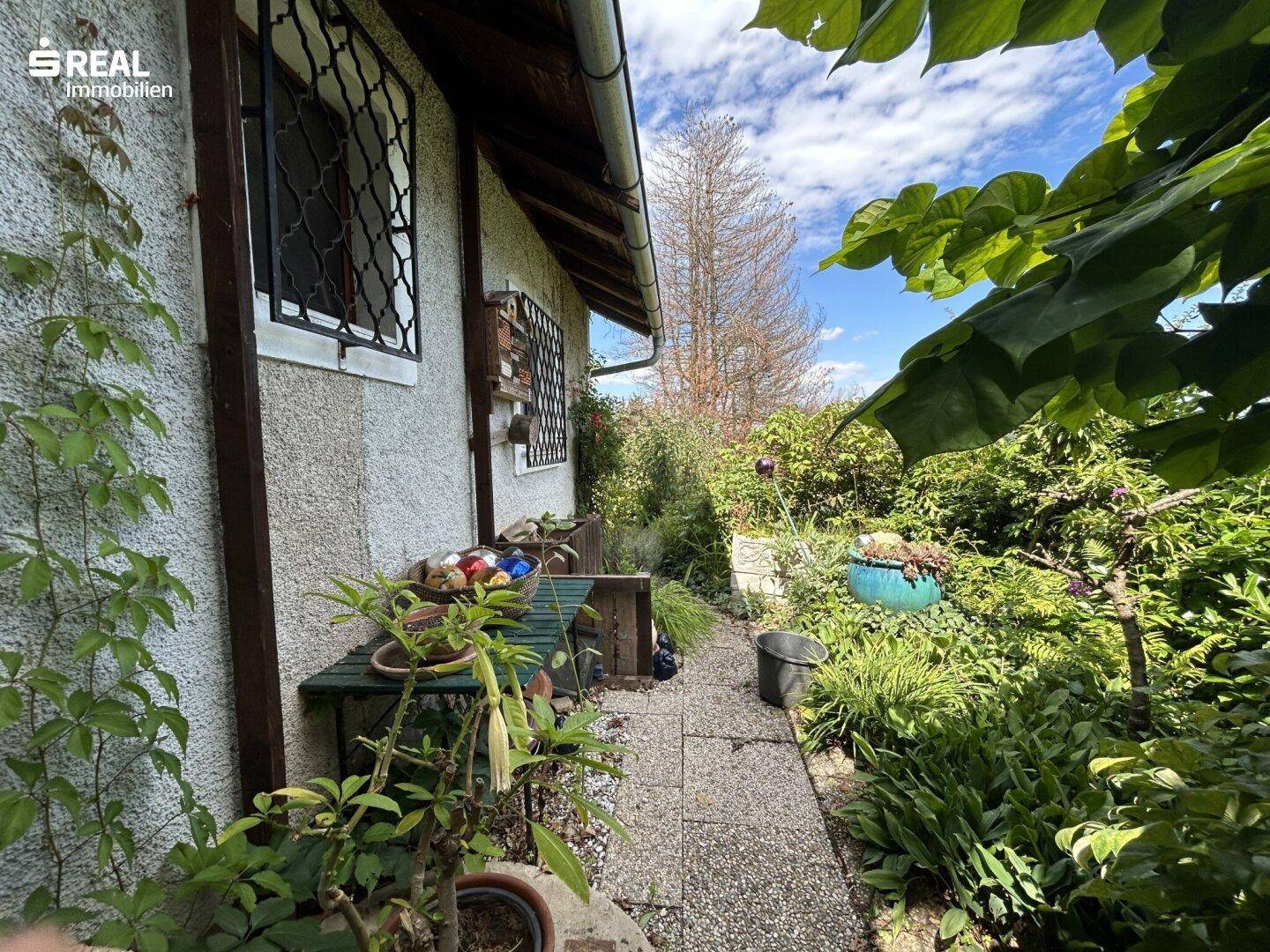 Seitlicher Gartenbereich mit üppiger Bepflanzung und einem schmalen Weg entlang des Hauses.