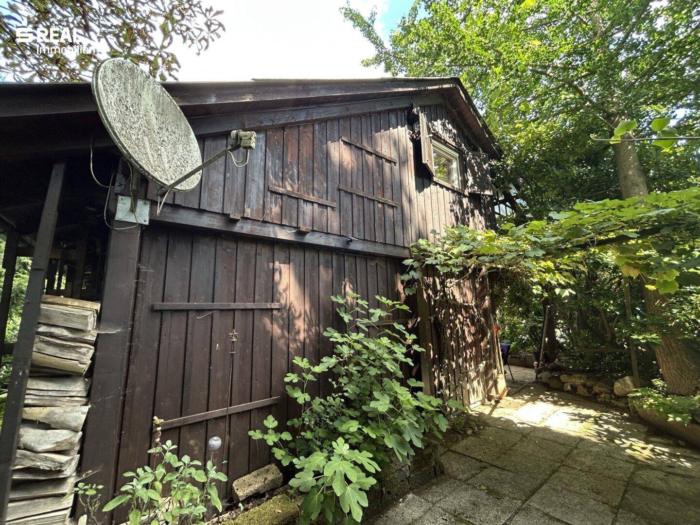 Rustikale Holzfassade eines Nebengebäudes mit Satellitenschüssel und viel Grün.