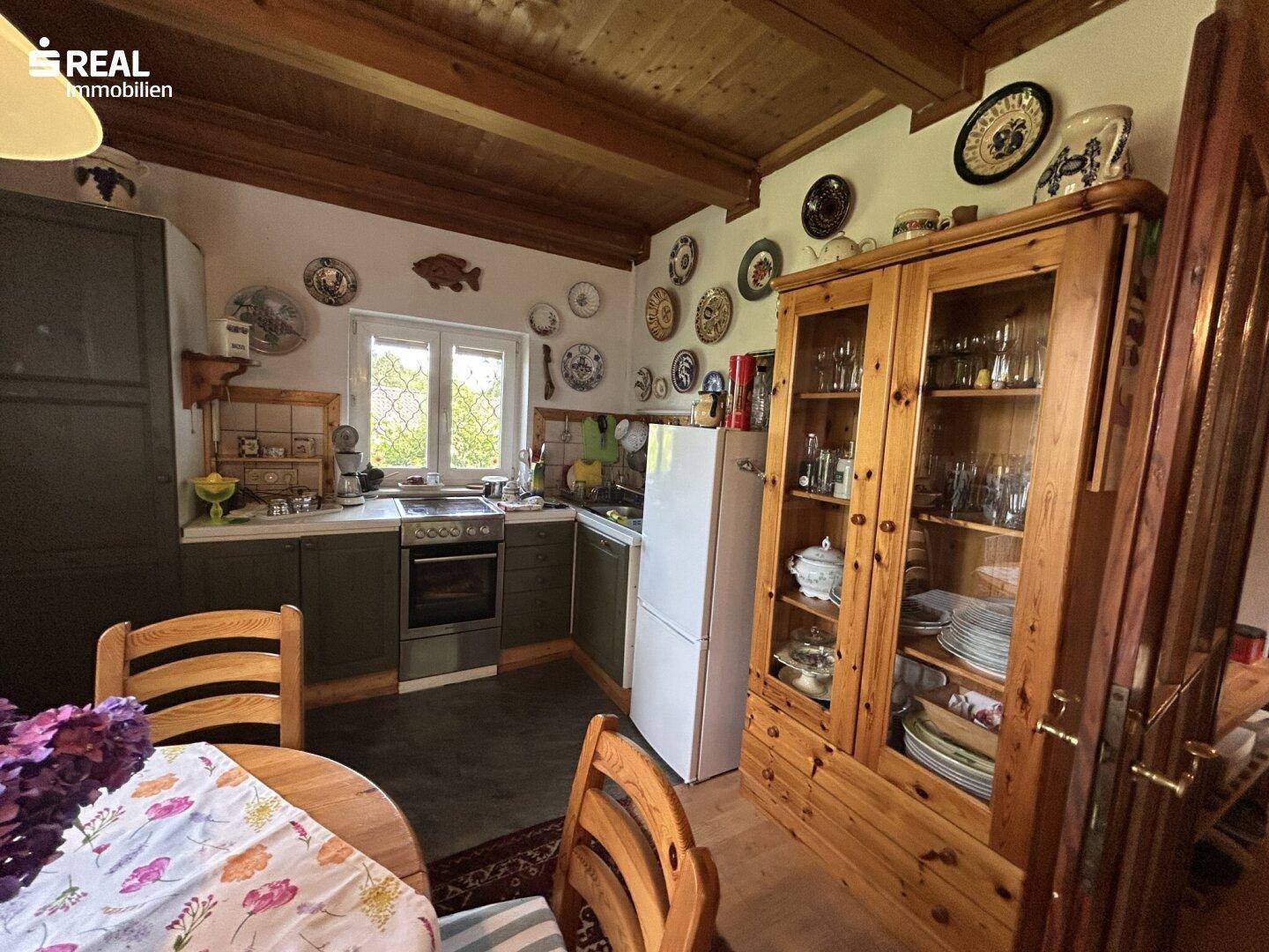 Traditionelle Küche mit Holzelementen, Essbereich und Blick ins Grüne durch das Fenster.