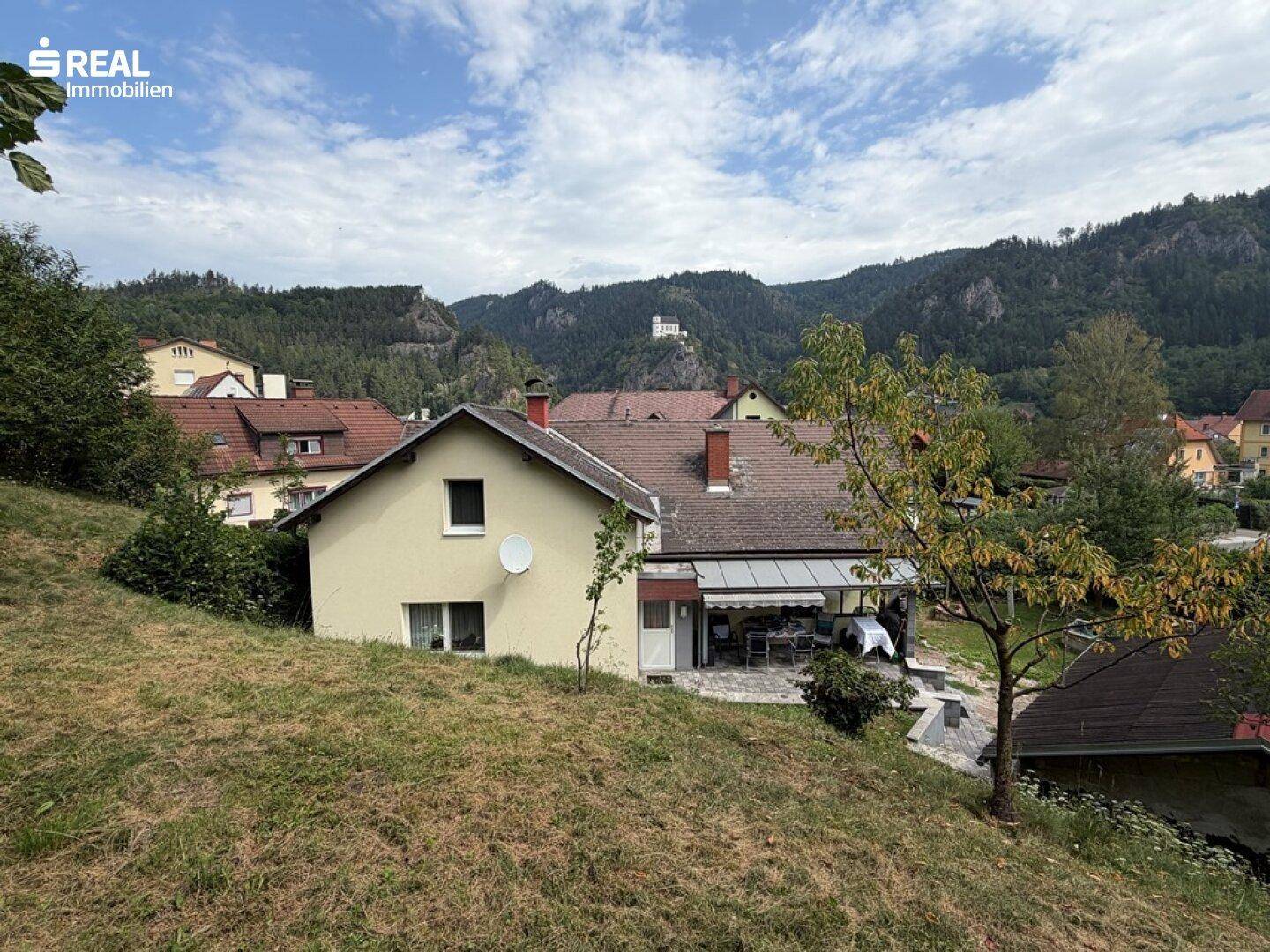 Weitläufiger Blick auf das Haus mit überdachter Terrasse und die malerische Bergkulisse im Hintergrund.