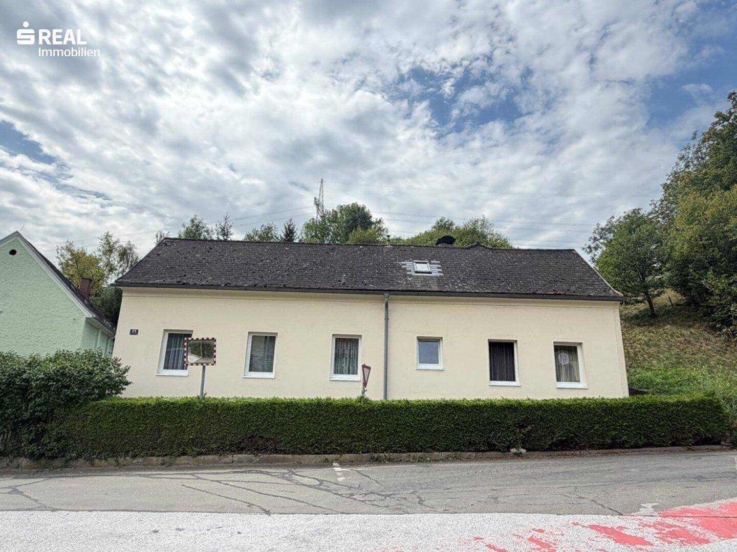 Frontansicht des Hauses mit mehreren Fenstern und einer gepflegten Hecke entlang der Straße.