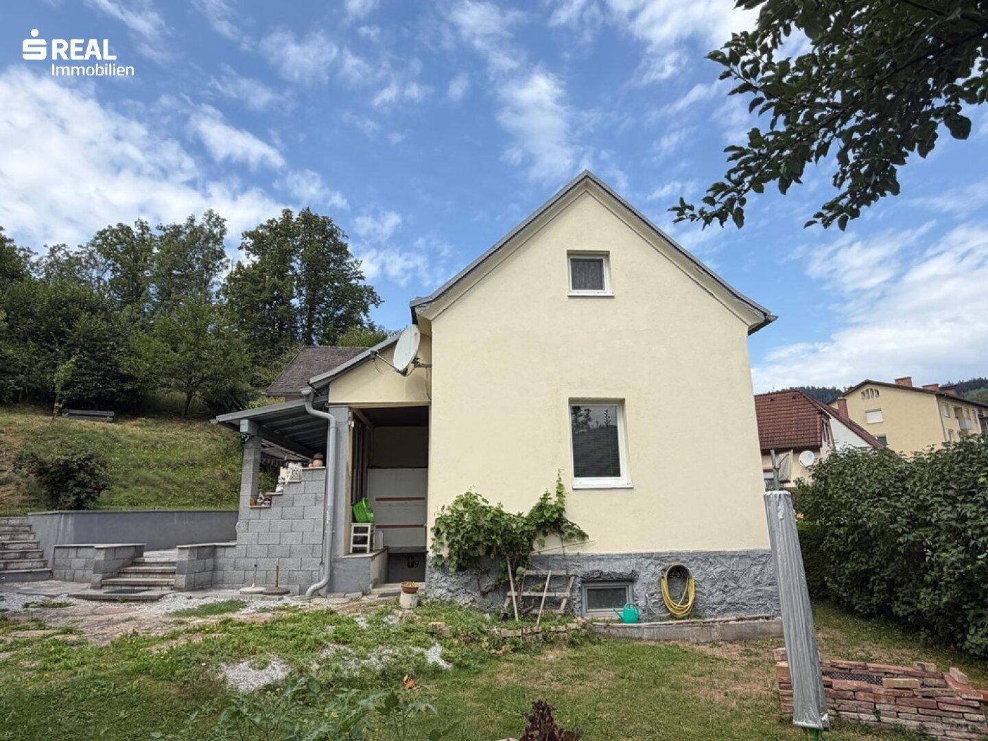 Seitenansicht des Hauses mit angrenzendem Gartenbereich und Blick auf die bewaldeten Hügel.