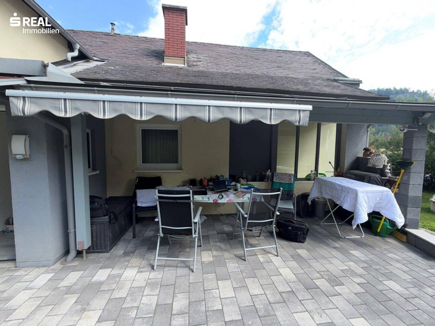 Überdachte Terrasse mit Gartenmöbeln, Markise und Blick auf die umliegende Natur.