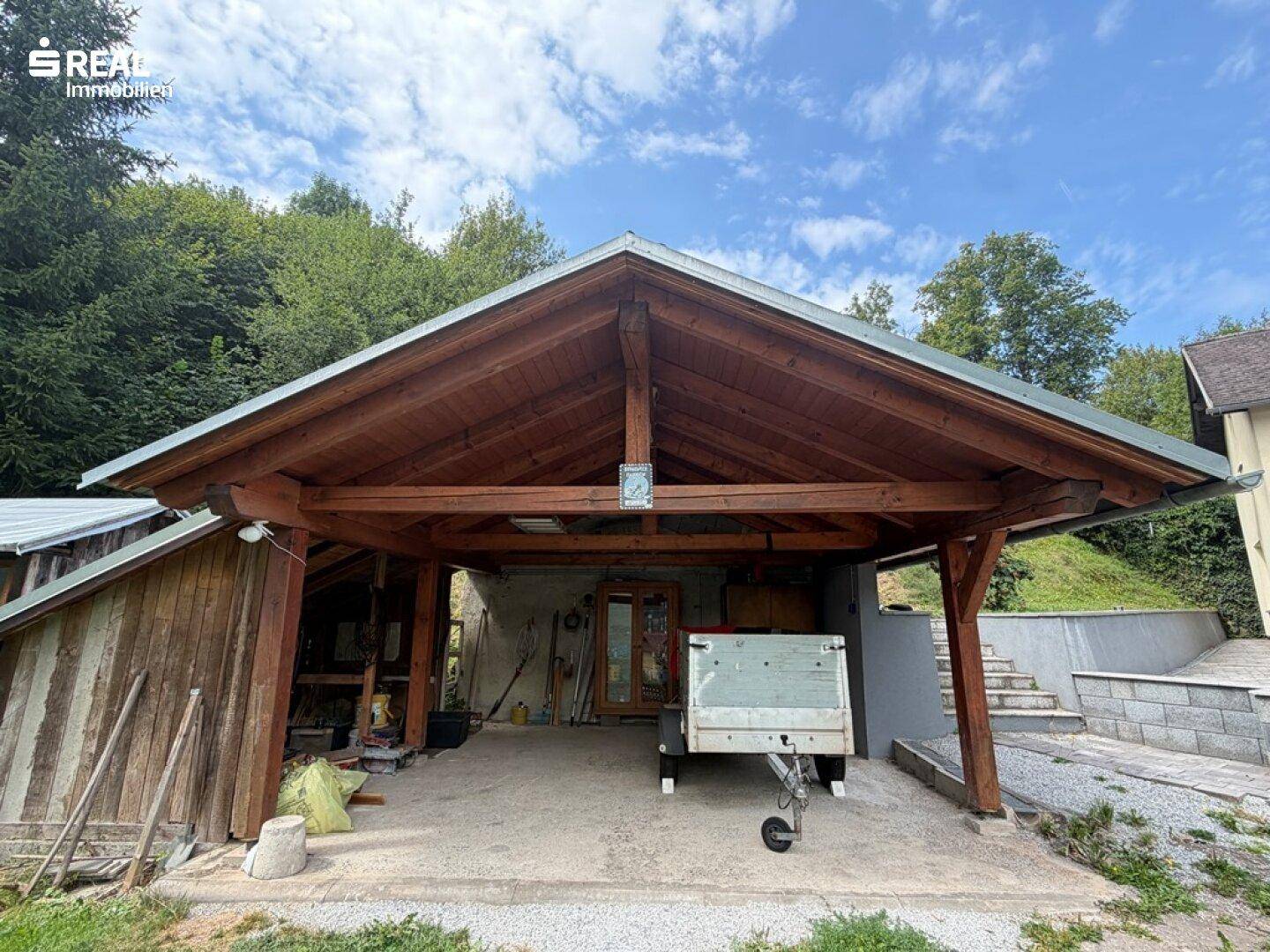 Geräumiger Holzcarport mit offenem Dachstuhl, bietet Schutz für Fahrzeuge und Lagerfläche.