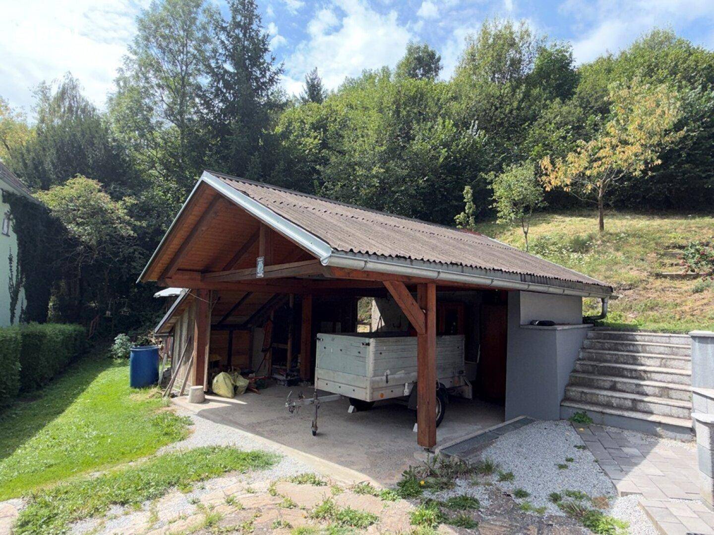 Ansicht des Holzcarports von der Seite mit angrenzendem Hang und Treppenaufgang.