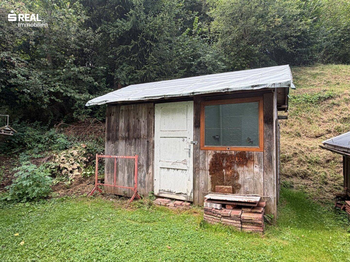 Rustikaler Holzschuppen im Gartenbereich mit Fenster und einfacher Holztür.