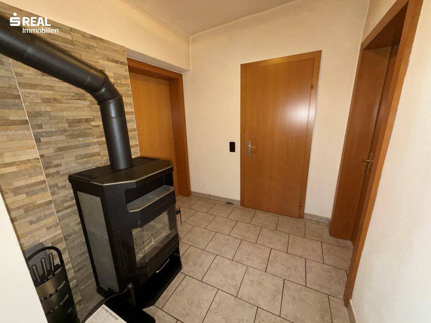 Flur mit modernem Holzofen vor einer Steinwand und Holztüren zu angrenzenden Räumen.