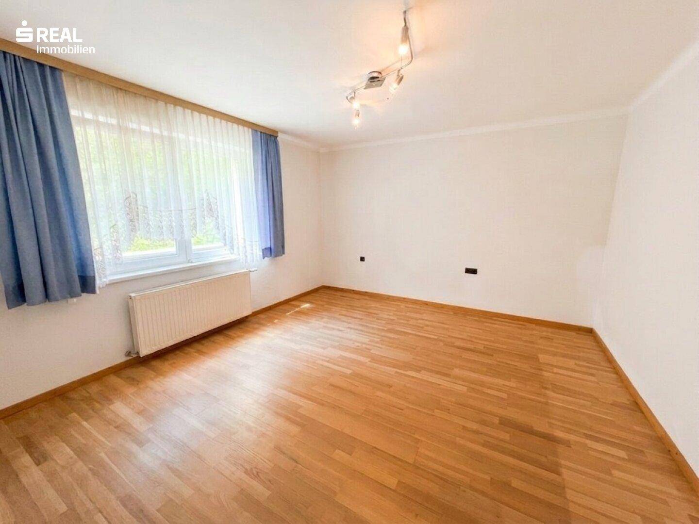 Helles Schlafzimmer mit Holzparkettboden, großem Fenster und Heizkörper.