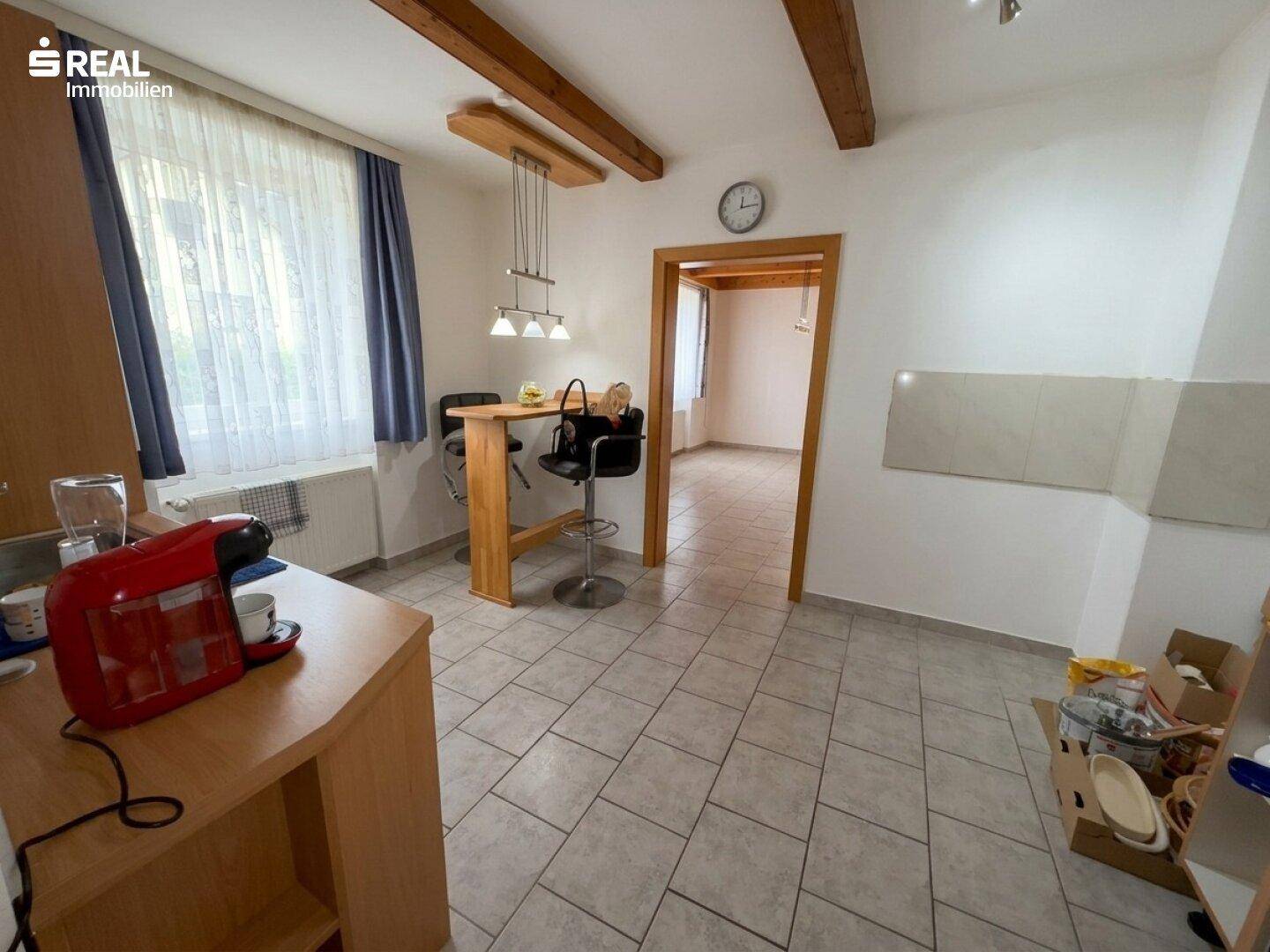 Küche mit Fliesenboden, Holzbalken und einem kleinen Bartresen, offen zu einem weiteren Raum.