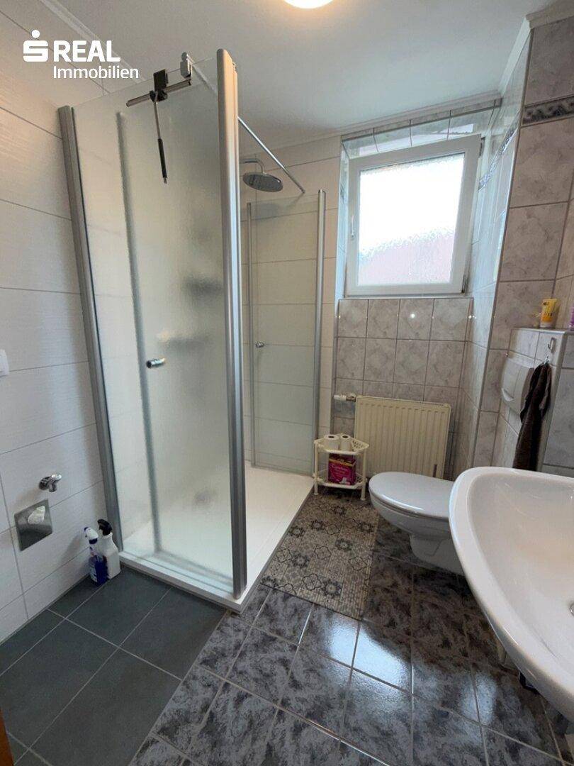 Helles Badezimmer mit Duschkabine, WC und Waschbecken, ausgestattet mit Fliesen und einem Fenster.