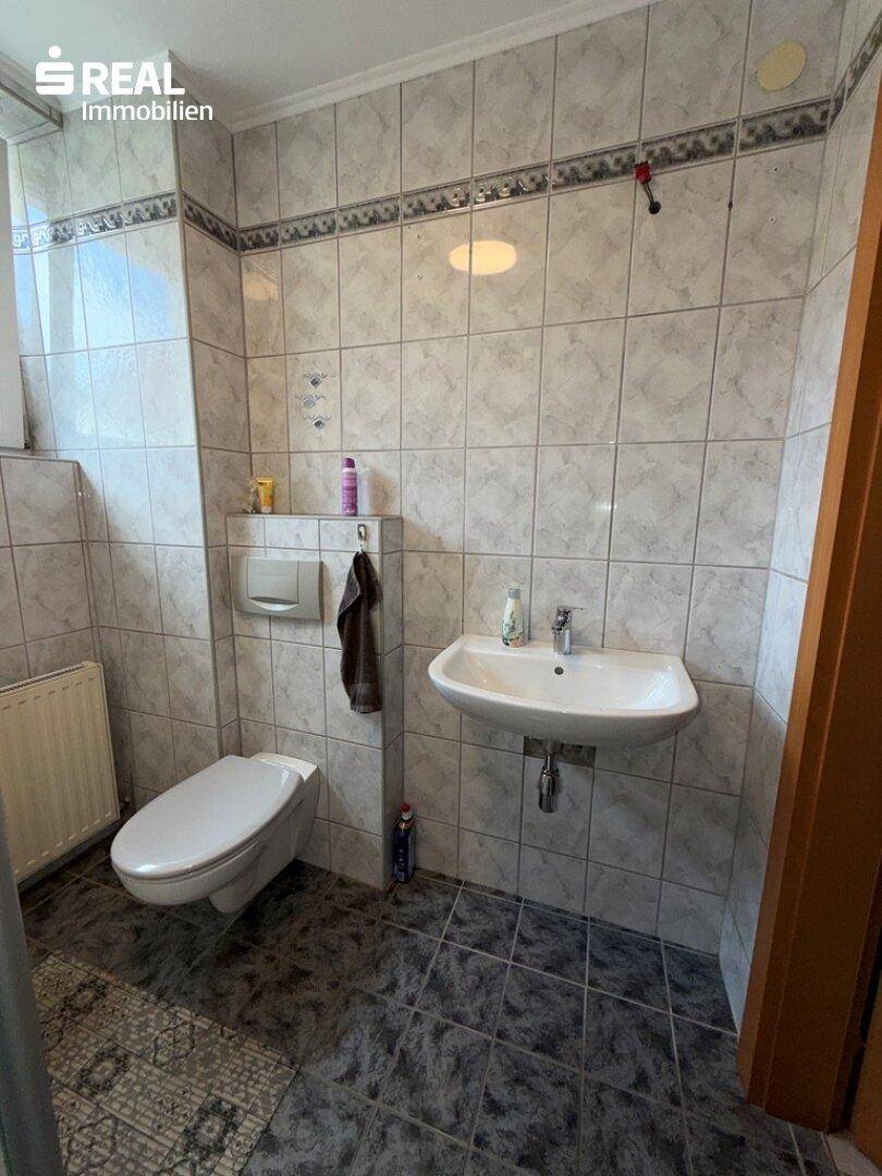 Funktionales Badezimmer mit Wand-WC, Waschbecken und gefliesten Wänden, gut beleuchtet durch ein Fenster.