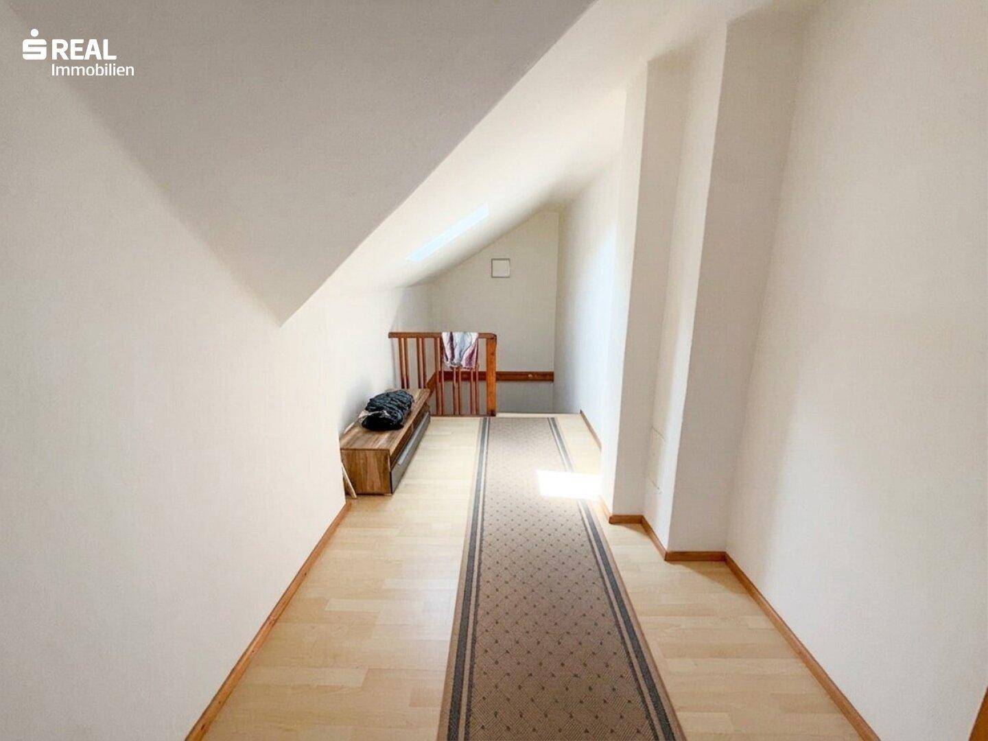 Heller Flur im Dachgeschoss mit Holzfußboden, schrägen Wänden und einer kleinen Sitzbank.