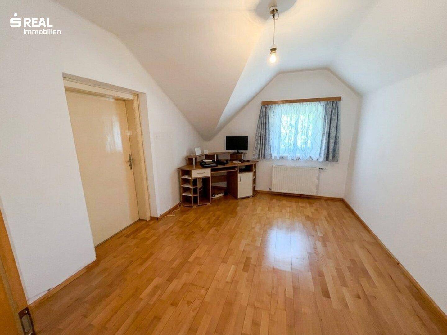 Geräumiges Zimmer im Dachgeschoss mit Holzfußboden, Fenster und Schreibtischbereich unter der Schräge.