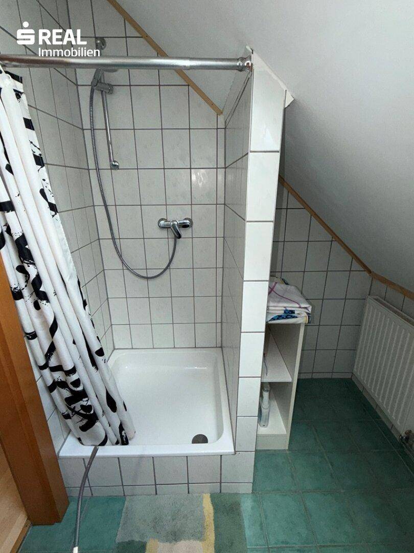 Badezimmer im Dachgeschoss mit Duschkabine, grünen Fliesen und schräger Decke.