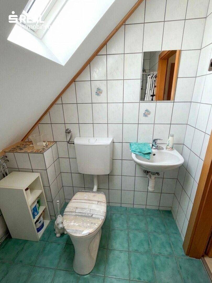 Dachgeschoss-Badezimmer mit WC, Waschbecken, Dachfenster und auffälligen grünen Fliesen.
