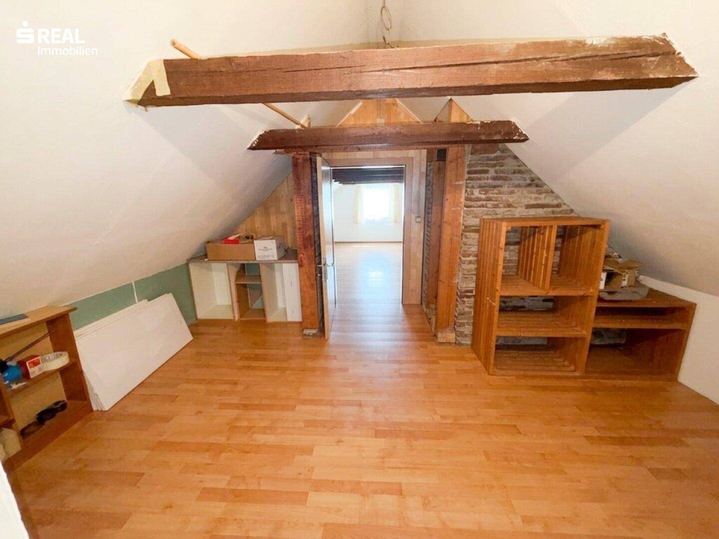Ausbaufähiger Dachbodenbereich mit sichtbaren Holzbalken und Zugang zu weiteren Räumen.