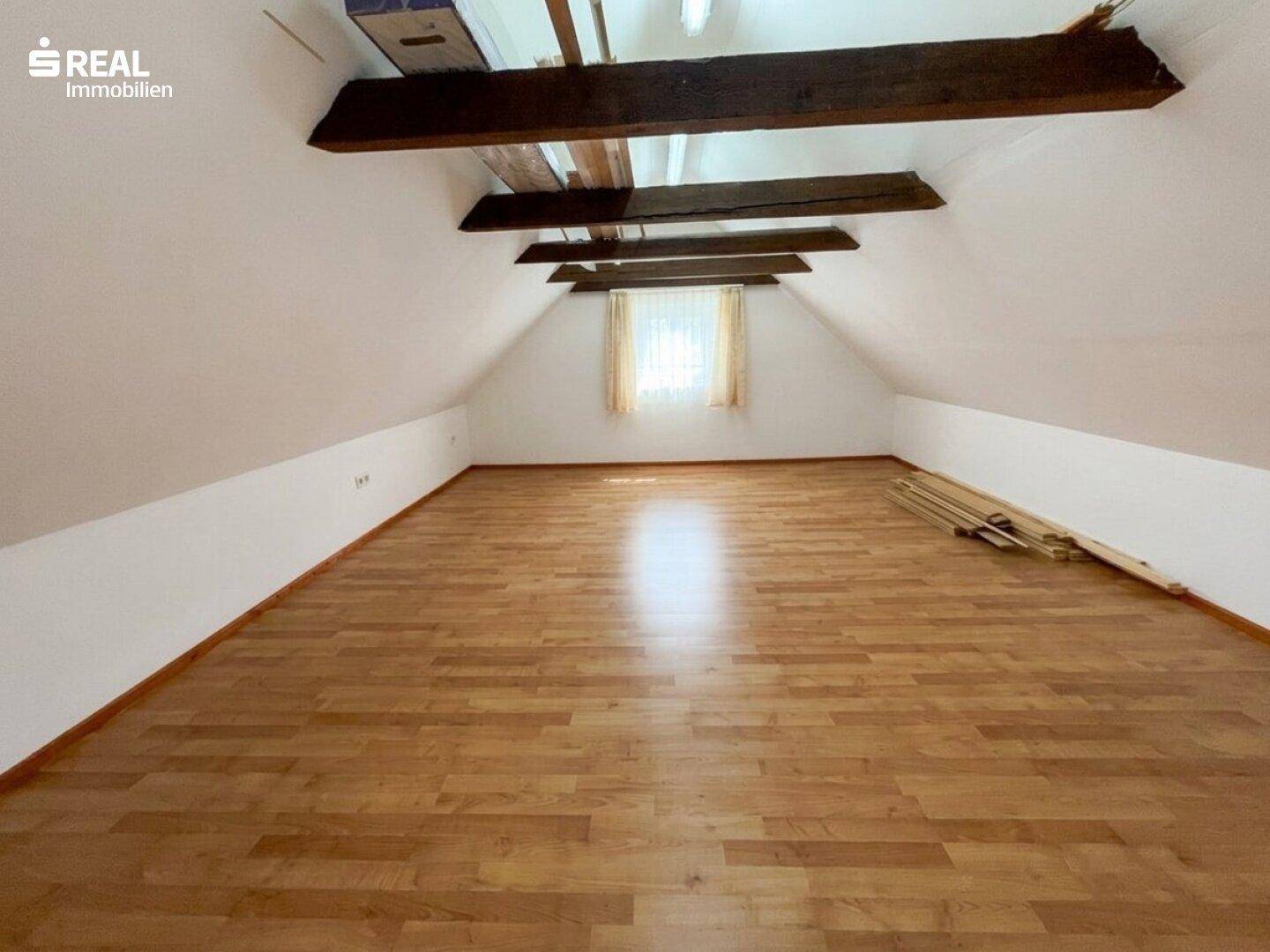 Geräumiger Dachboden mit Holzbalken, Fenster und Laminatboden, bietet Ausbaupotenzial.