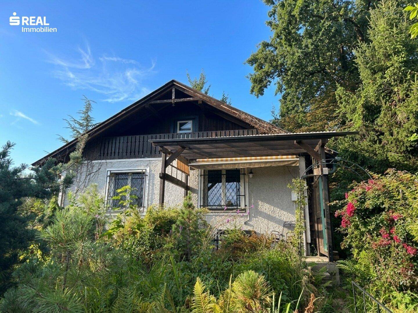 Ansicht des Hauses mit überdachtem Eingangsbereich und grüner Umgebung unter blauem Himmel.