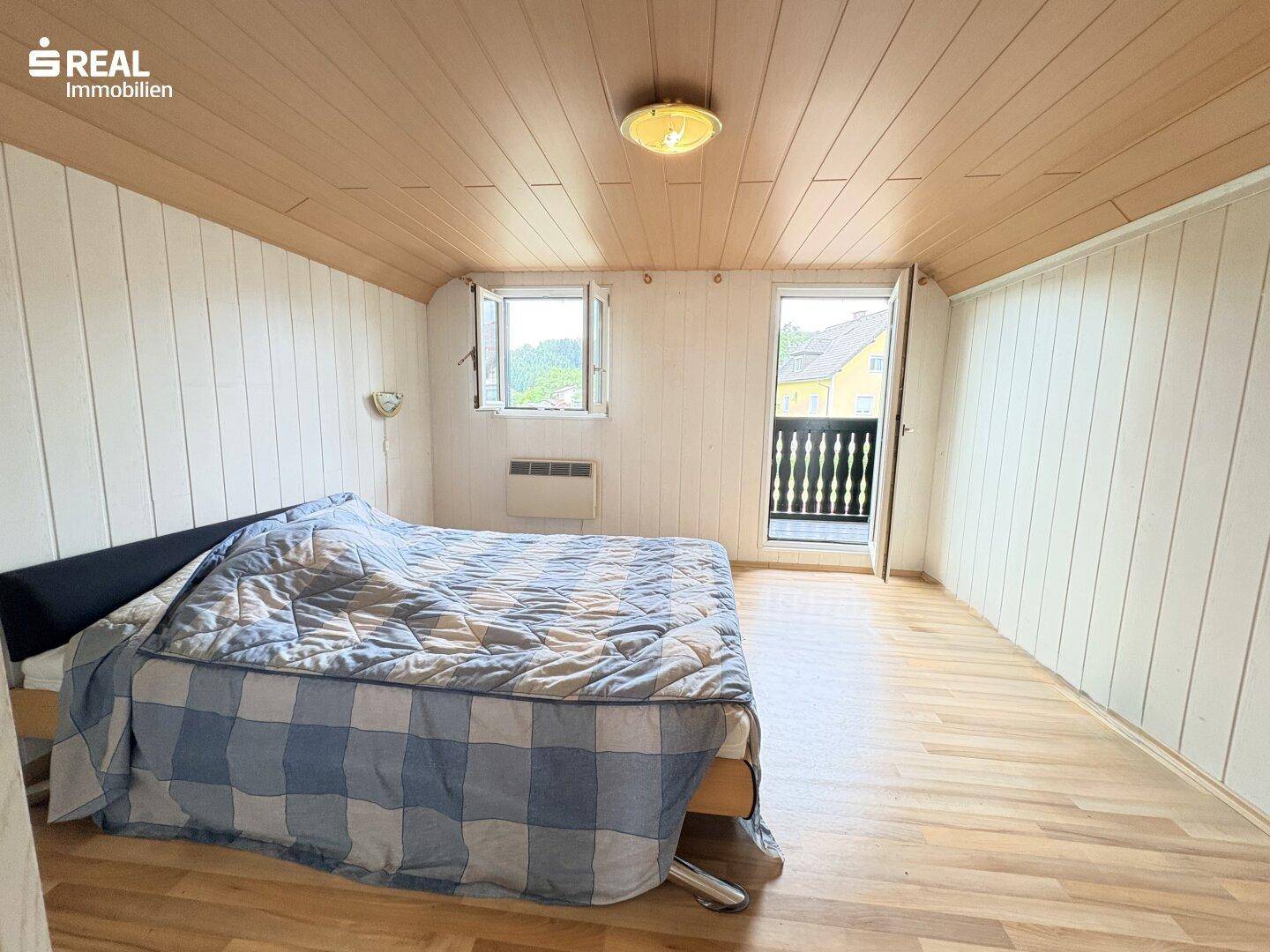 Schlafzimmer mit Holzwänden, Dachschräge und Zugang zu einem französischen Balkon.
