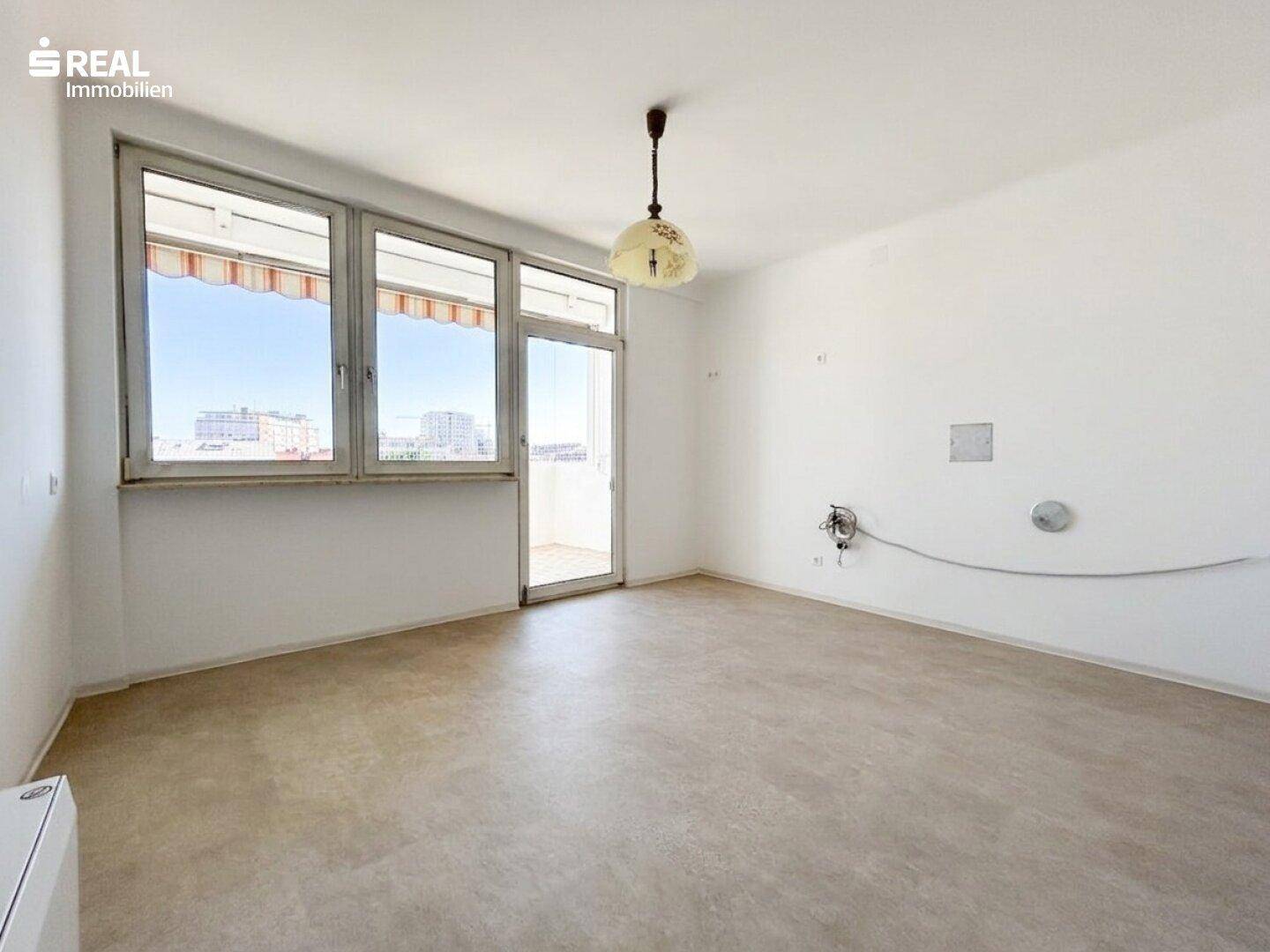 Heller Raum mit schlichtem Bodenbelag und Zugang zum Balkon, bietet einen Blick auf die Stadt.