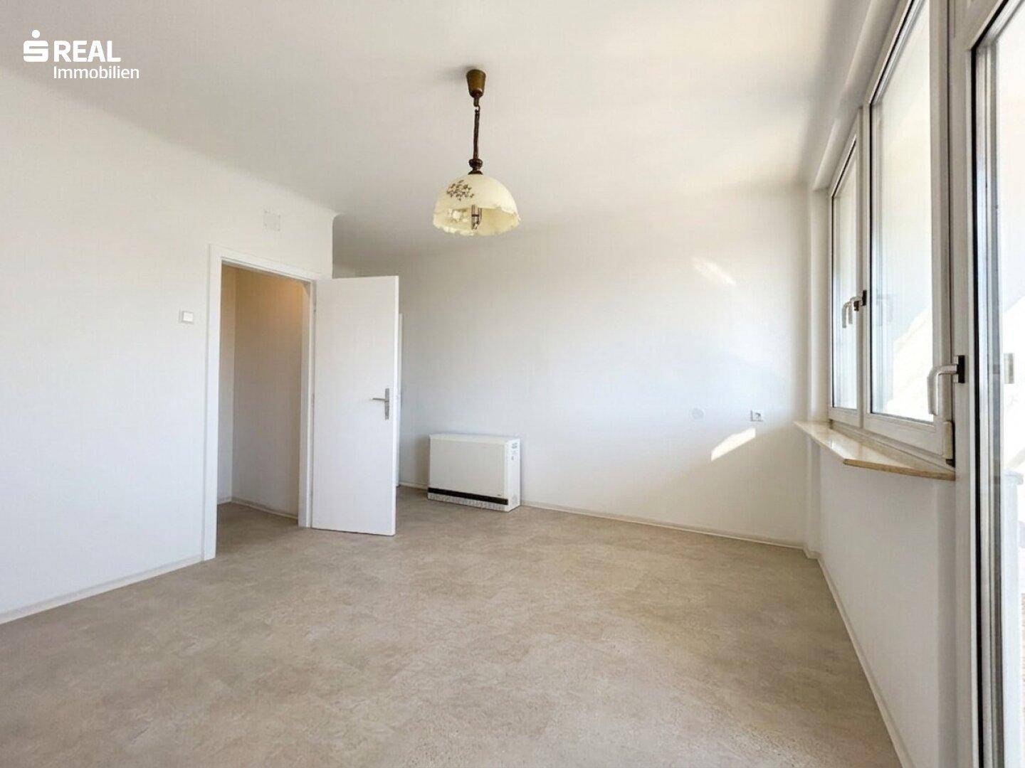 Helles Zimmer mit großen Fenstern, Heizkörper und schlichtem Bodenbelag, ideal für individuelle Gestaltung.