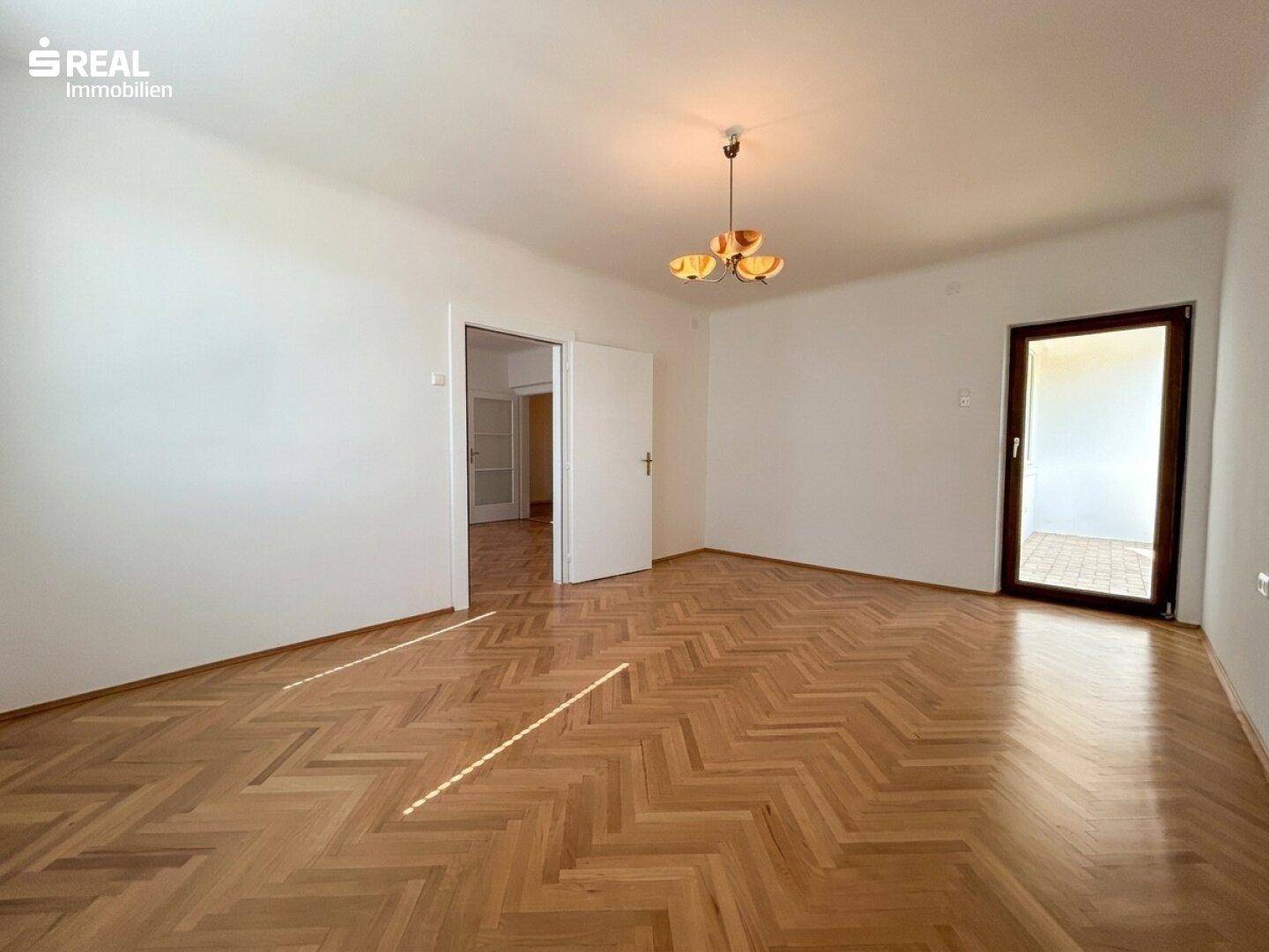 Geräumiges Zimmer mit Fischgrätparkett und direktem Zugang zu einem Außenbereich, ideal für sonnige Tage.