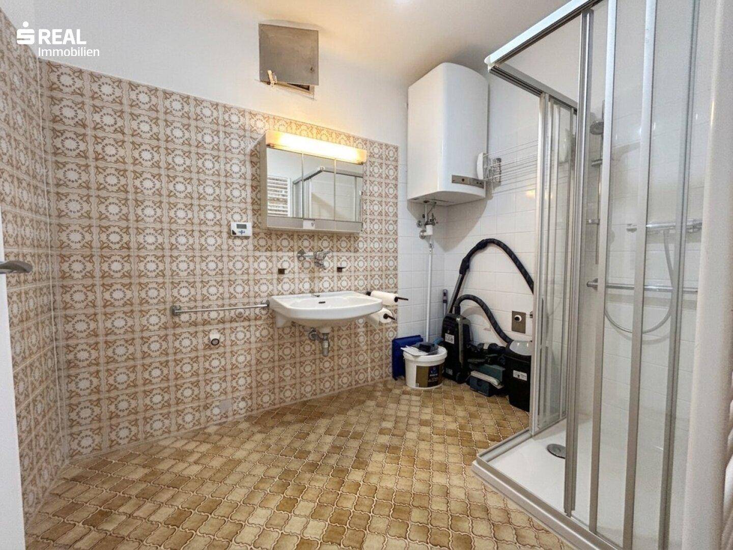 Badezimmer mit gemusterten Fliesen, Duschkabine und Waschbecken, ausgestattet mit einem Spiegelschrank.