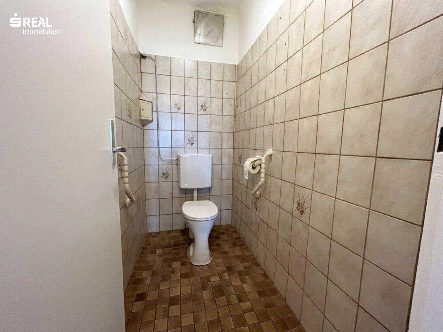 Separate Toilette mit gemusterten Fliesen und einem Wand-WC, funktional und sauber gehalten.