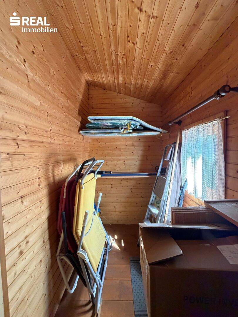 Kleiner Abstellraum mit Holzverkleidung, Fenster und Stauraum für verschiedene Gegenstände.