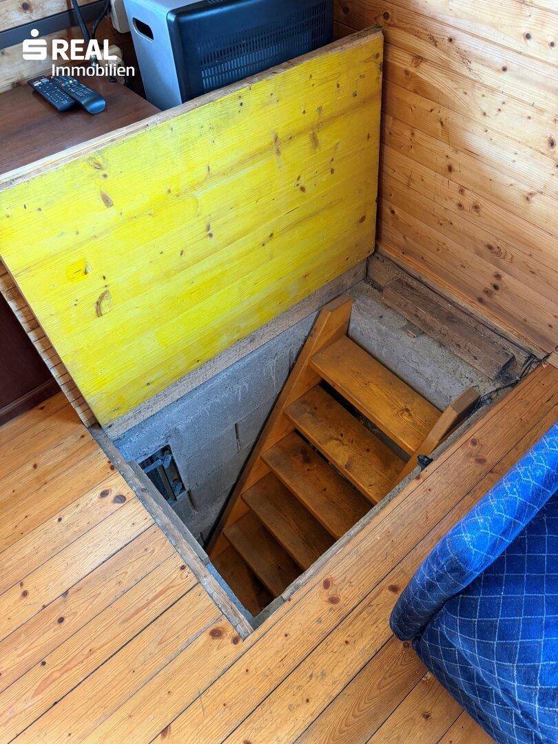 Holzluke im Boden führt über eine Treppe hinunter in den Kellerbereich des Hauses.