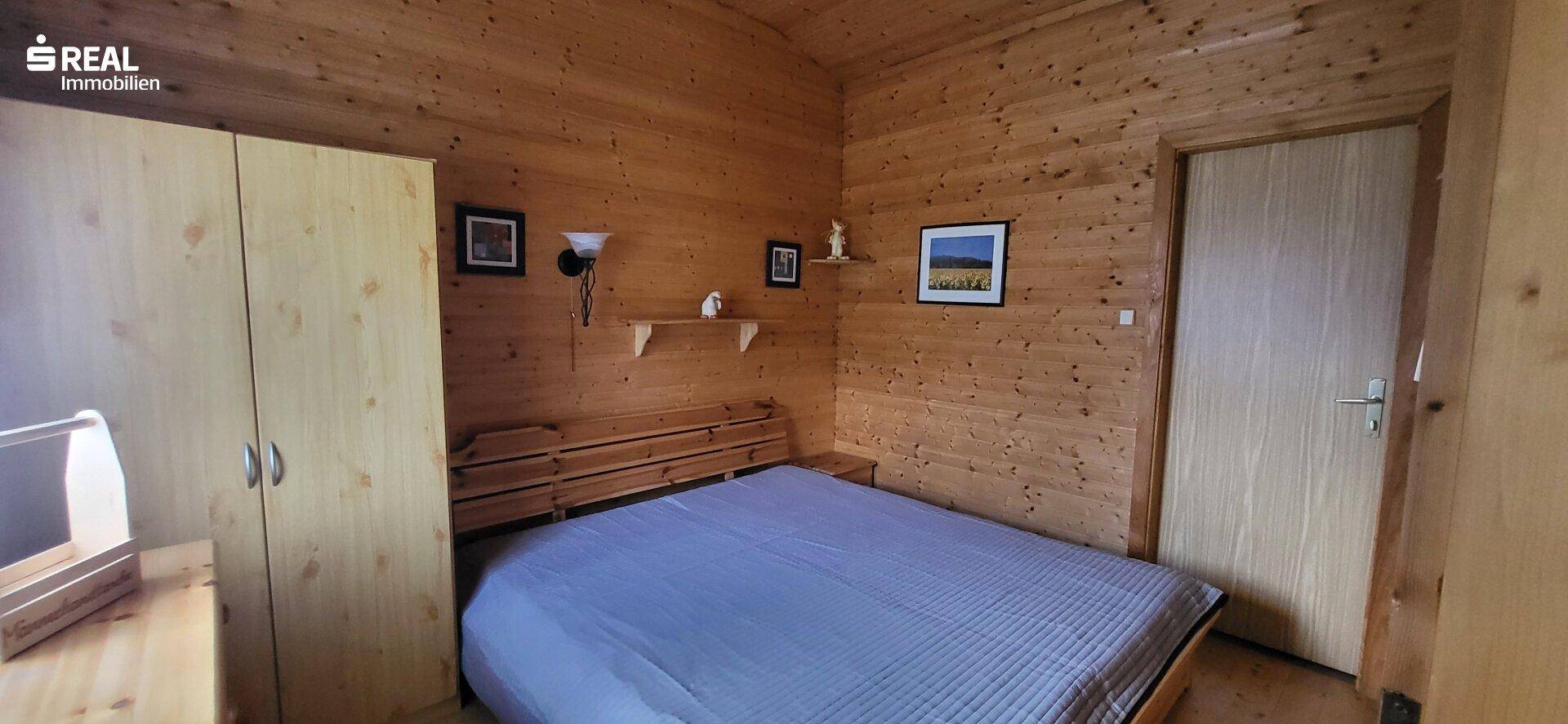 Schlafzimmer mit Holztäfelung an Wänden und Decke, Doppelbett und hellem Holzschrank.