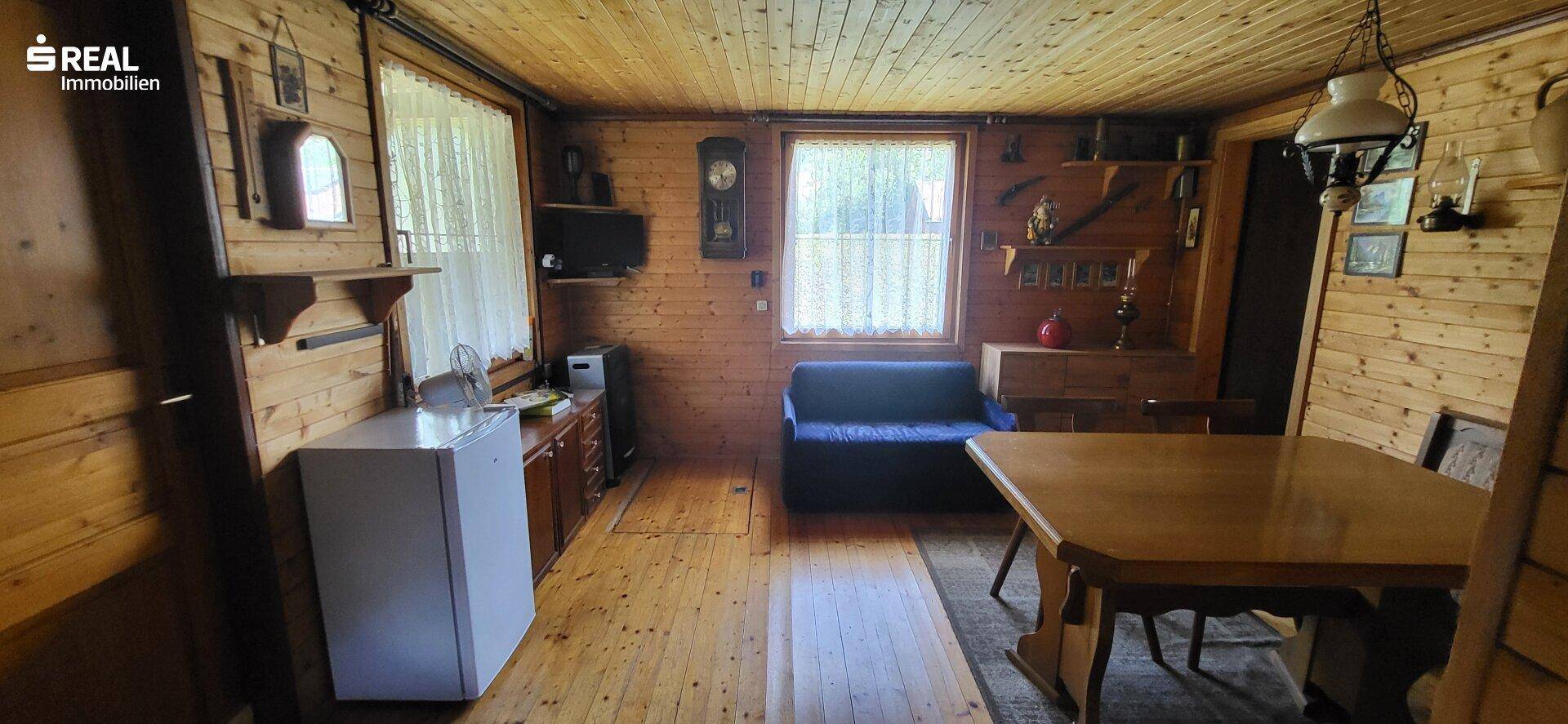 Rustikaler Wohnbereich mit Holzboden, Esstisch und kleiner Sitzecke, durchflutet von natürlichem Licht.