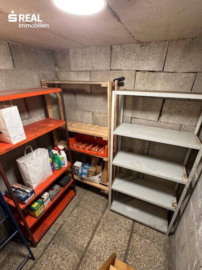 Kellerraum mit Betonsteinwänden und verschiedenen Regalen für Lagerzwecke.