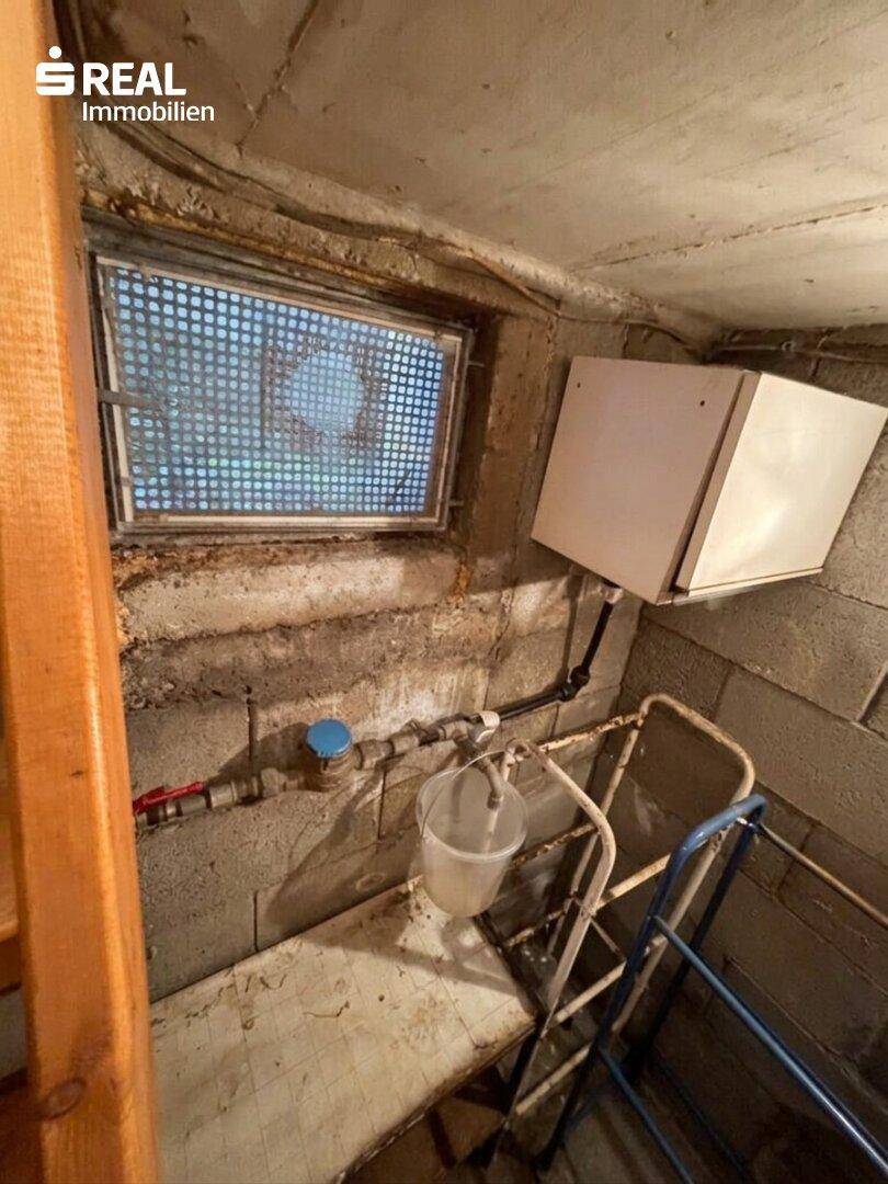Kellerraum mit Betonsteinwänden, kleinem Fenster und sichtbaren Wasserleitungen.