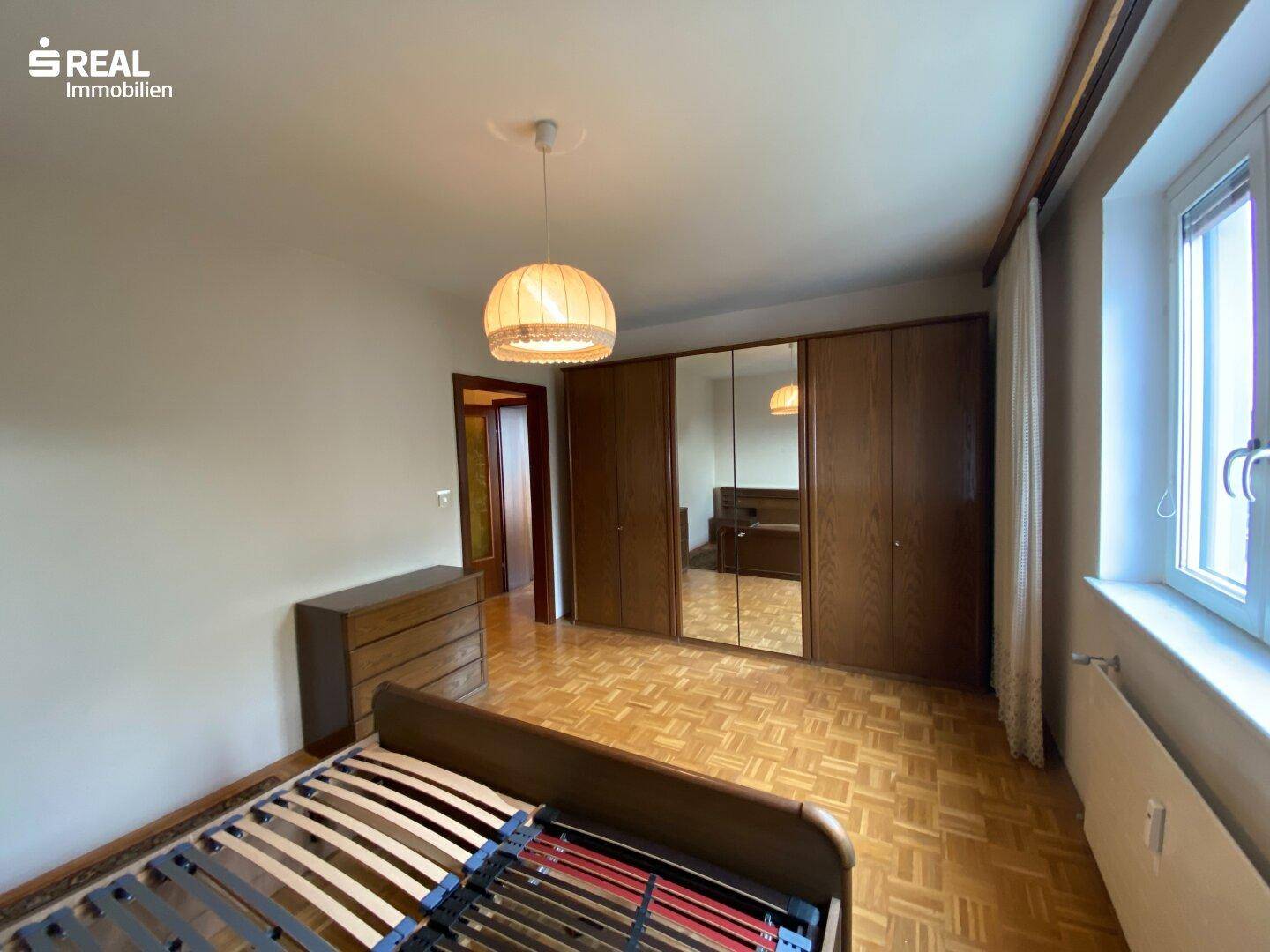 Schlafzimmer mit Parkettboden, großem Spiegelschrank und Fenster für natürliches Licht.