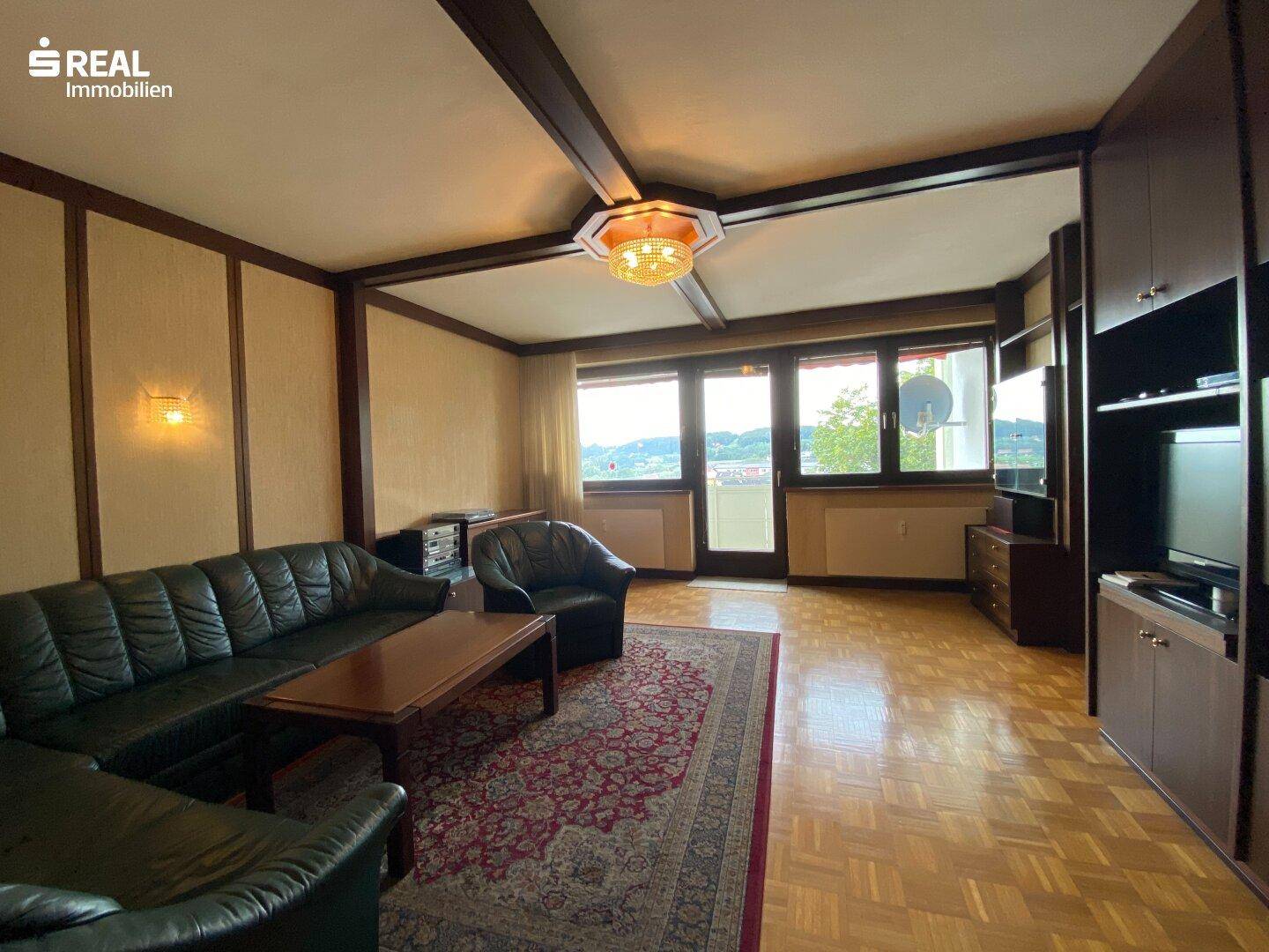 Gemütliches Wohnzimmer mit dunklen Ledersofas, Parkettboden und Holzbalken an der Decke.