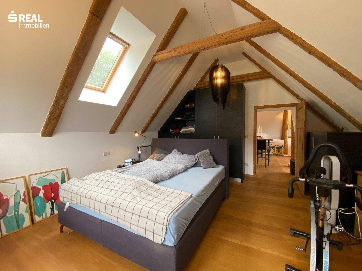 Gemütliches Schlafzimmer im Dachgeschoss mit Holzbalken, Dachfenster und Holzboden.