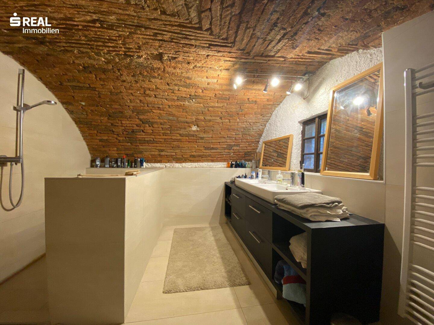Einzigartiges Badezimmer mit freiliegender Ziegeldecke, Doppelwaschbecken und moderner Dusche.