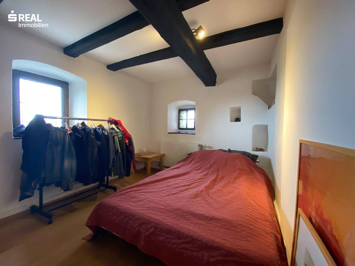 Rustikales Schlafzimmer mit dunklen Holzbalken, weiß gestrichenen Wänden und Holzboden.