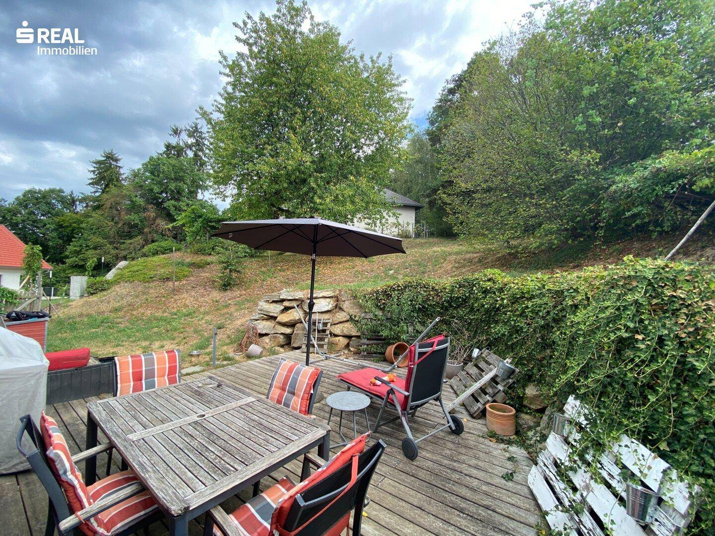 Holzterrasse mit Gartenmöbeln, Sonnenschirm und Blick auf den Gartenbereich.