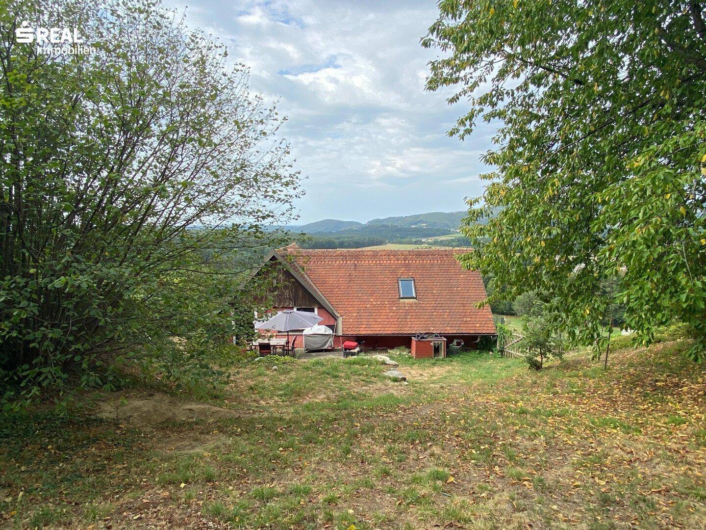 Das Haus eingebettet in eine grüne Hügellandschaft unter bewölktem Himmel.