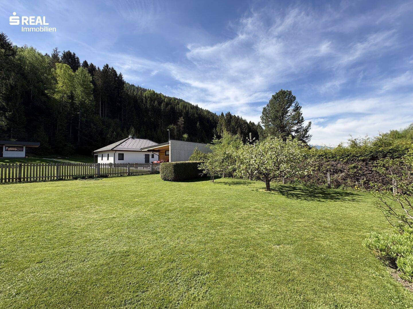 Weitläufiger Rasenbereich mit Obstbäumen und Blick auf den Waldrand und ein weiteres Haus.